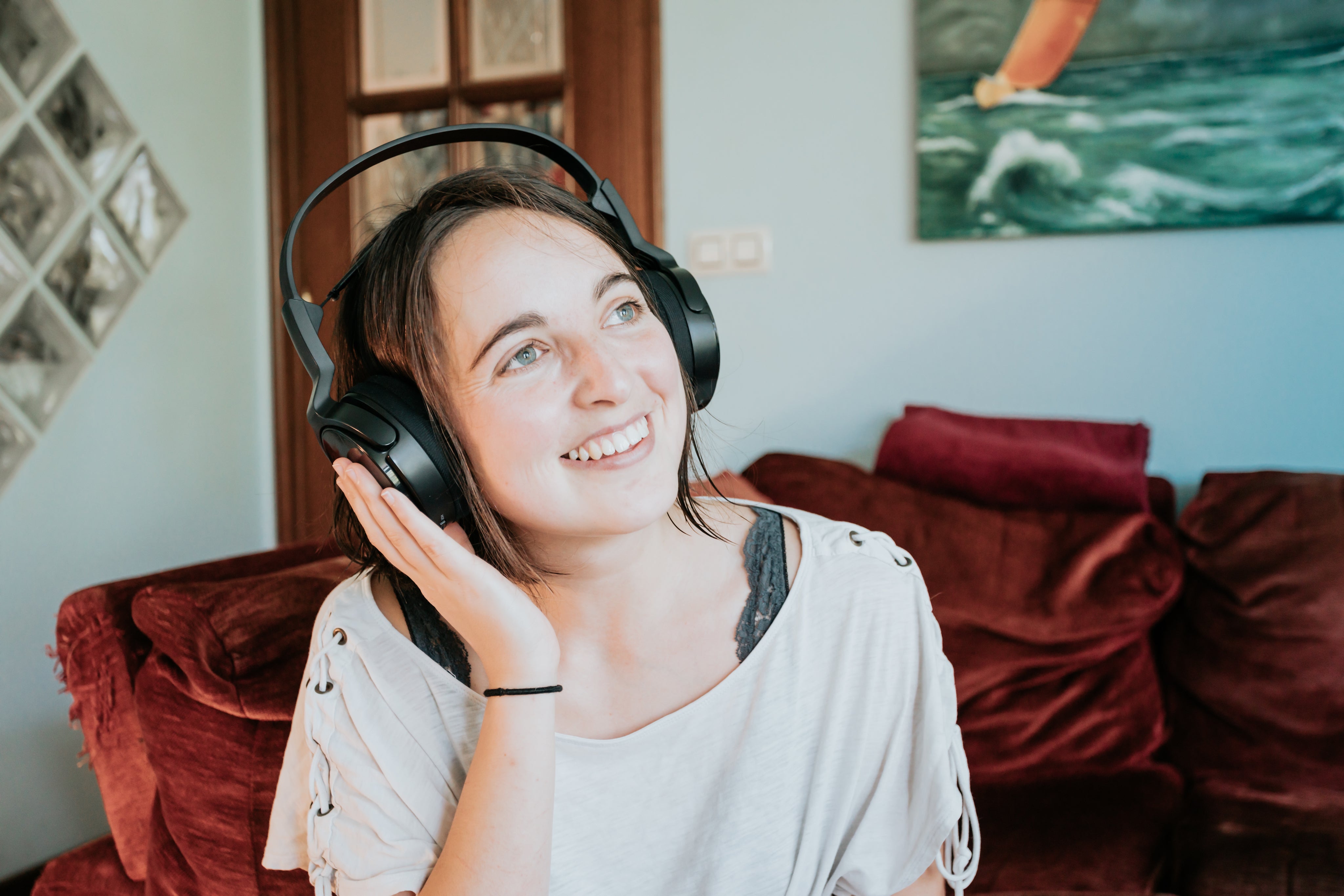 A young woman wears headphones in a comfortable room and smiles.